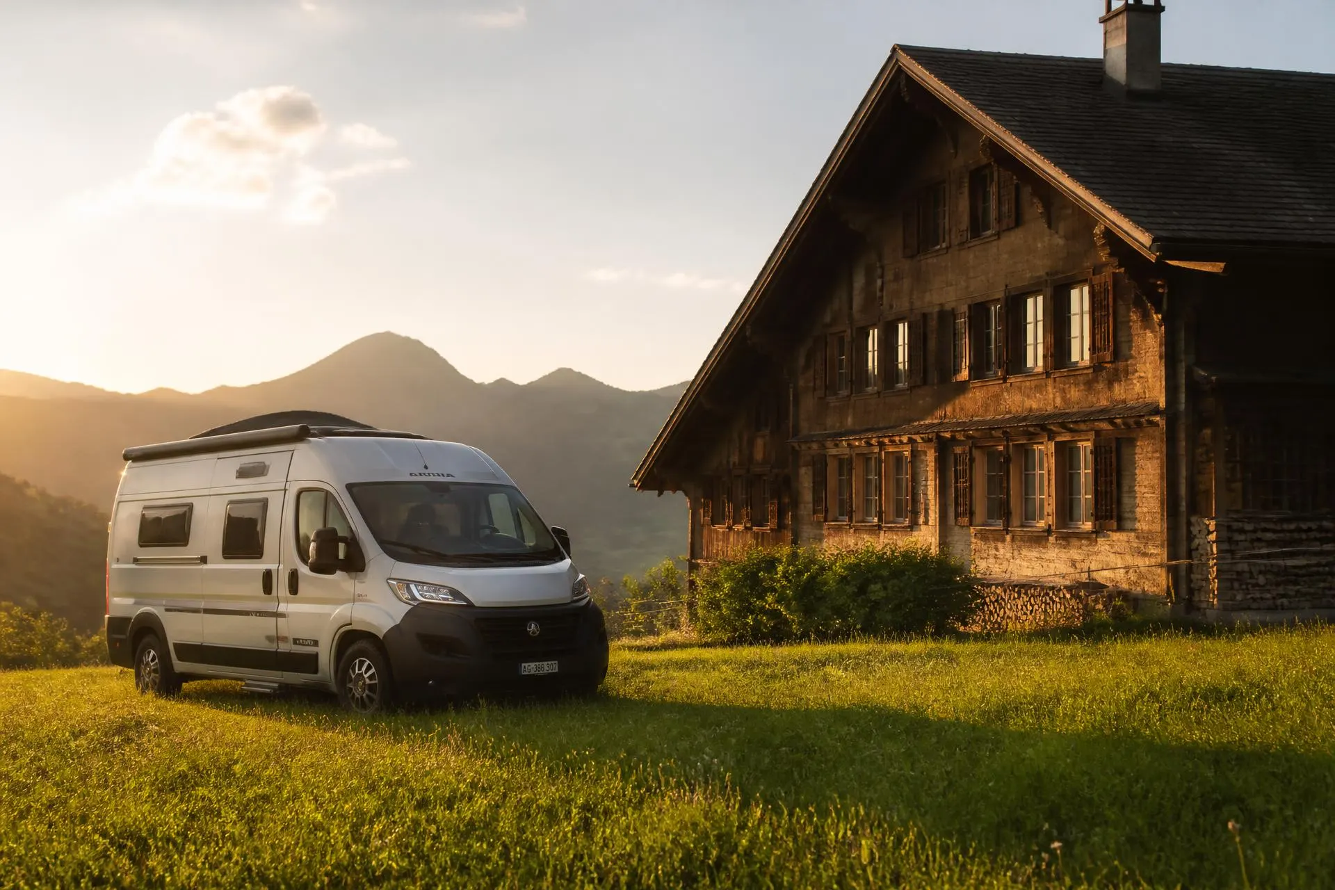 Camper-Übernachtungsplatz bei einem Schweizer Bauernhof Camper auf einer Wiese neben einem Schweizer Bauernhaus im Abendlicht